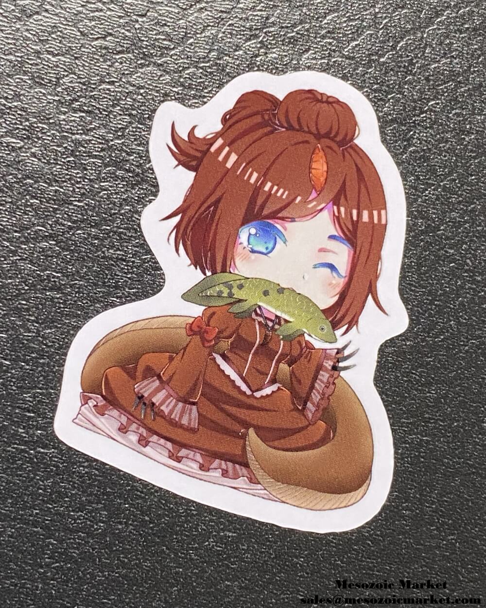 Type B variant of a vinyl sticker of our Spinosaurus anime girl mascot eating a lungfish placed on a display box.